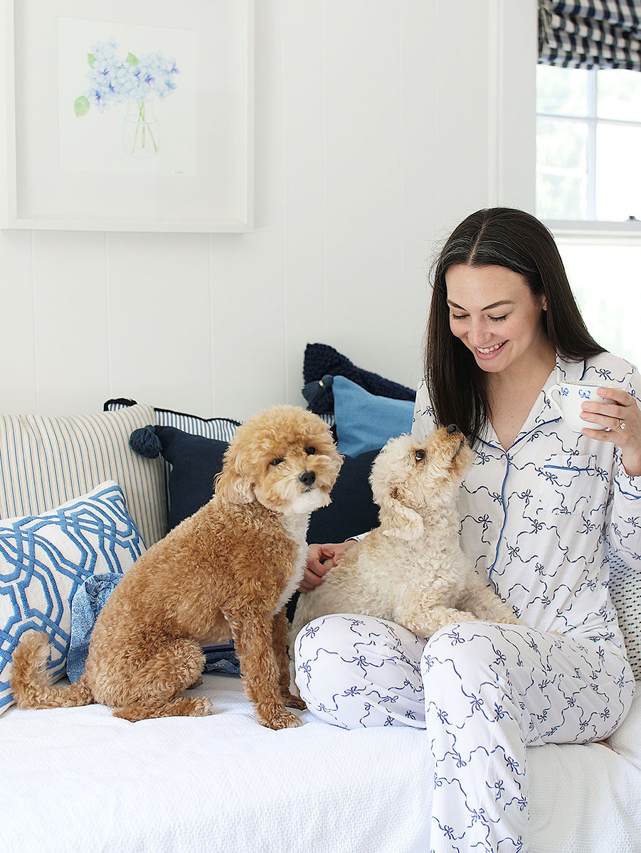 Carly Heitlinger sits on the daybed in her office wearing pajamas with her two dogs and a cup of coffee!