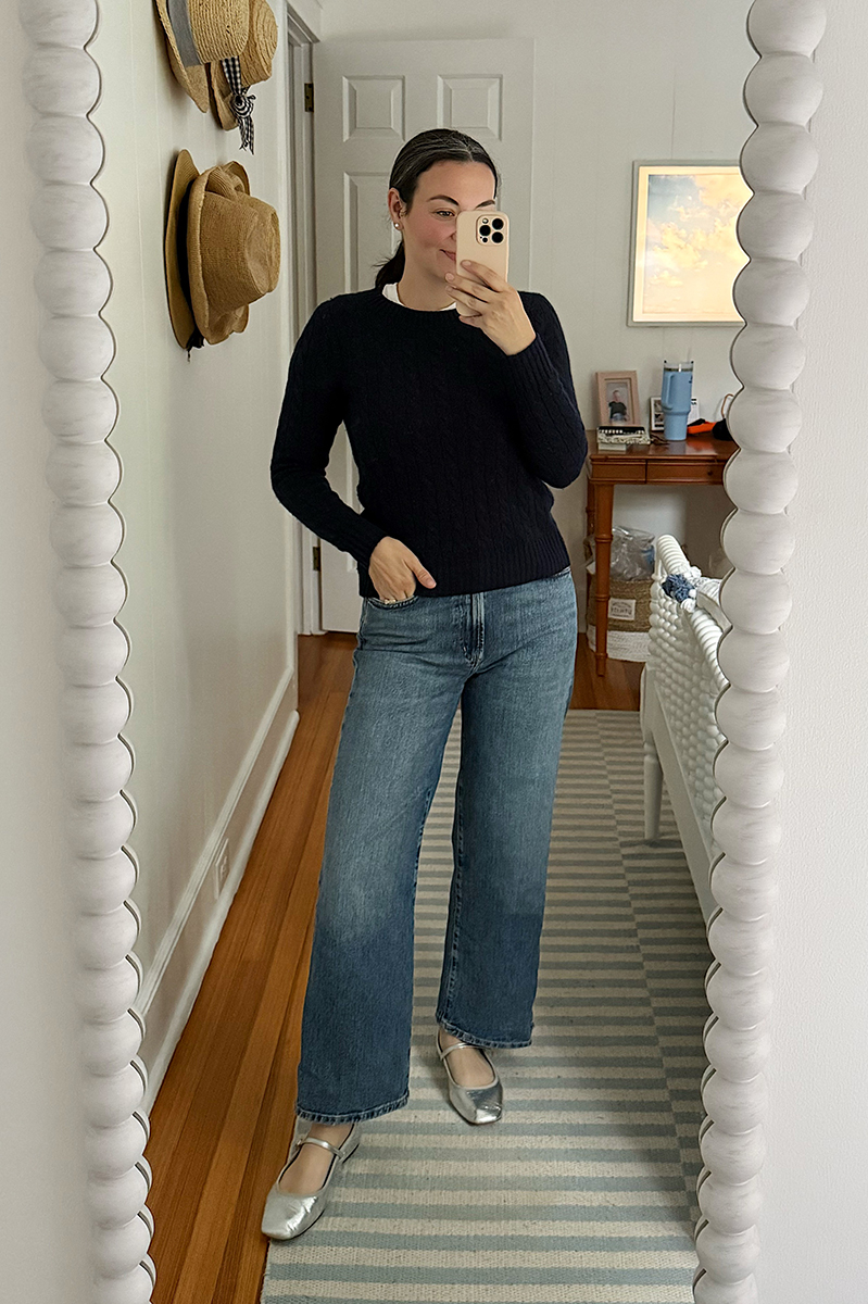 Carly Riordan taking a mirror selfie wearing a navy sweater and wide leg jeans.