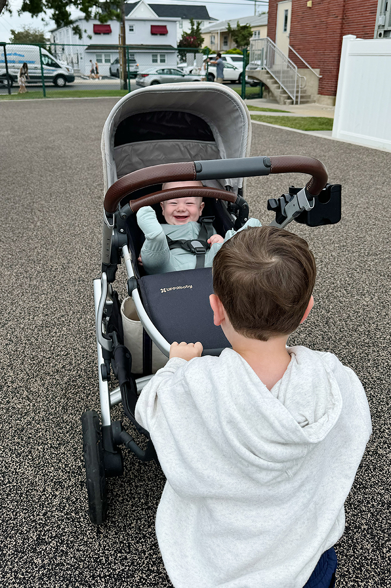 A toddler boy pushing a baby in a stroller