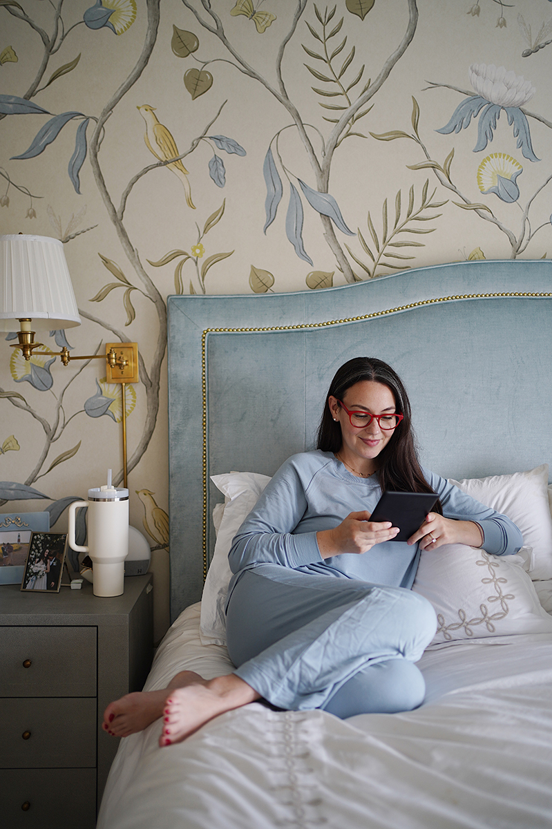 Carly Riordan on her bed wearing blue loungewear reading her kindle