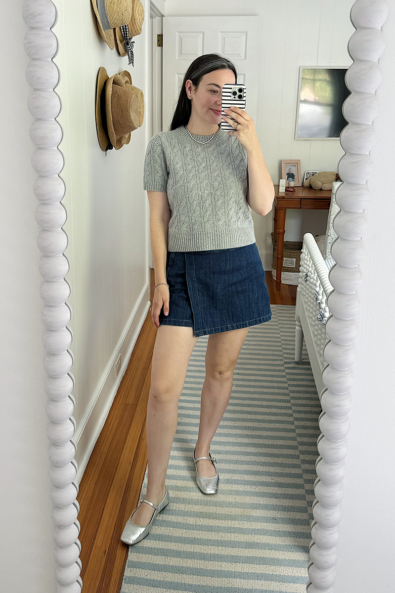 Carly Riordan taking a mirror selfie wearing a short sleeve sweater and denim skort.