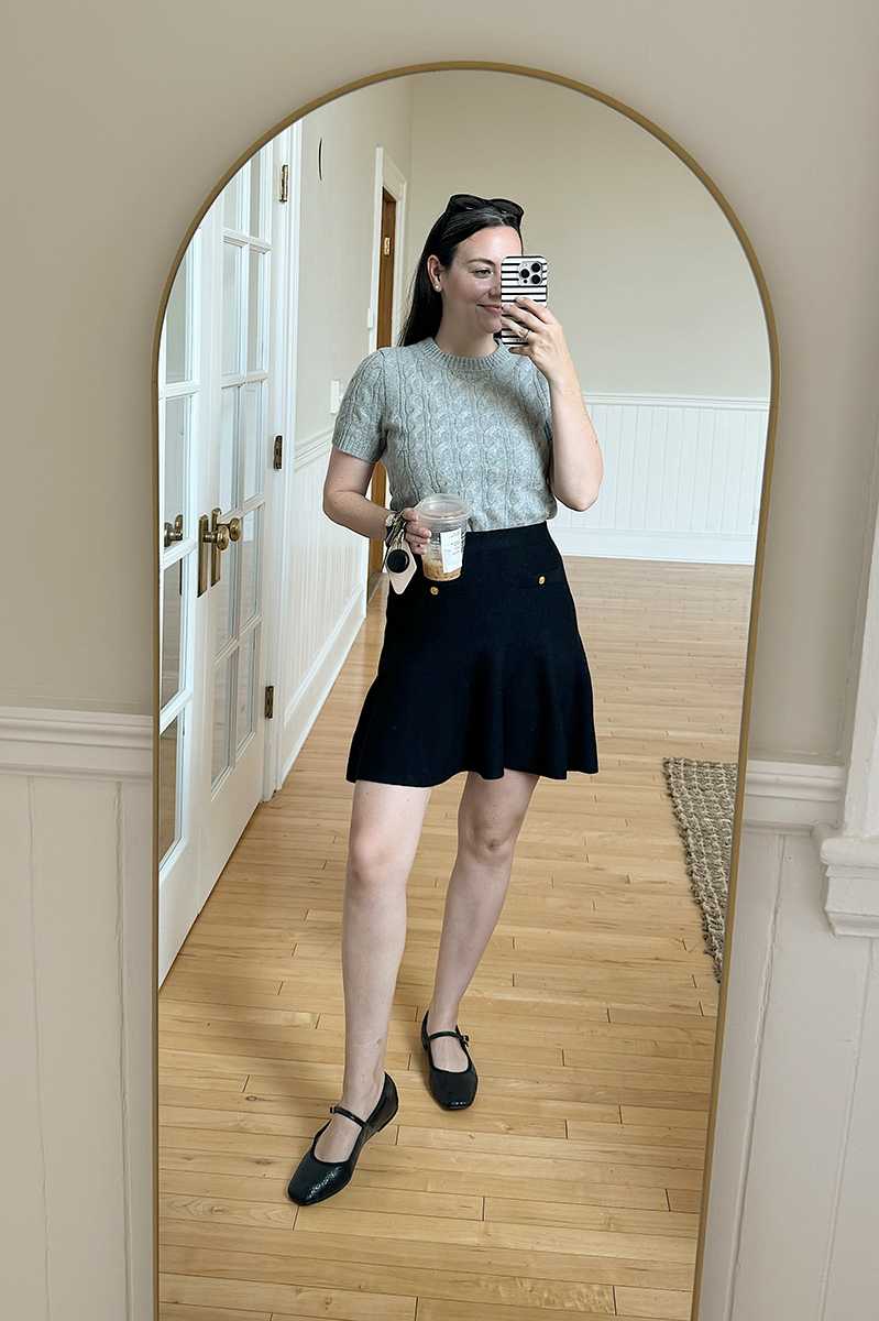 Carly taking a mirror selfie wearing a grey sweater and black knit skirt.