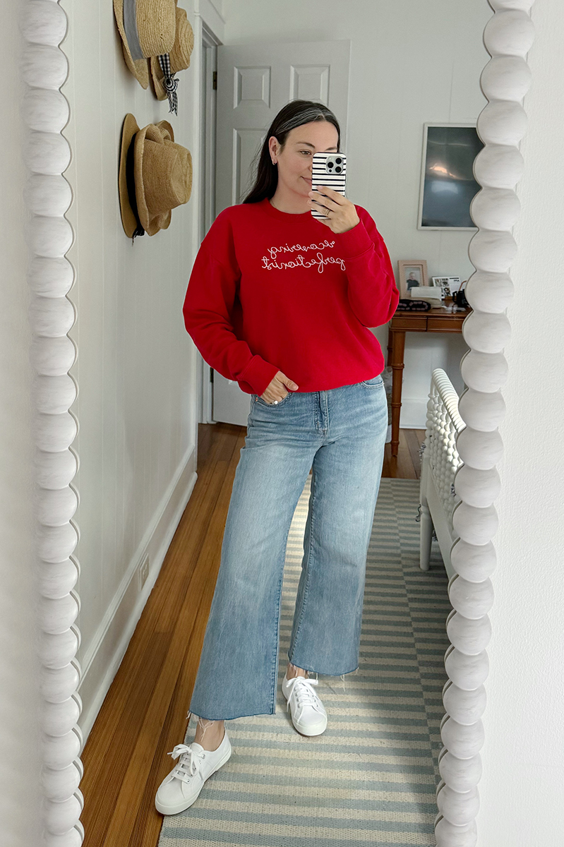 Carly taking a mirror selfie wearing denim jeans and a red sweatshirt.