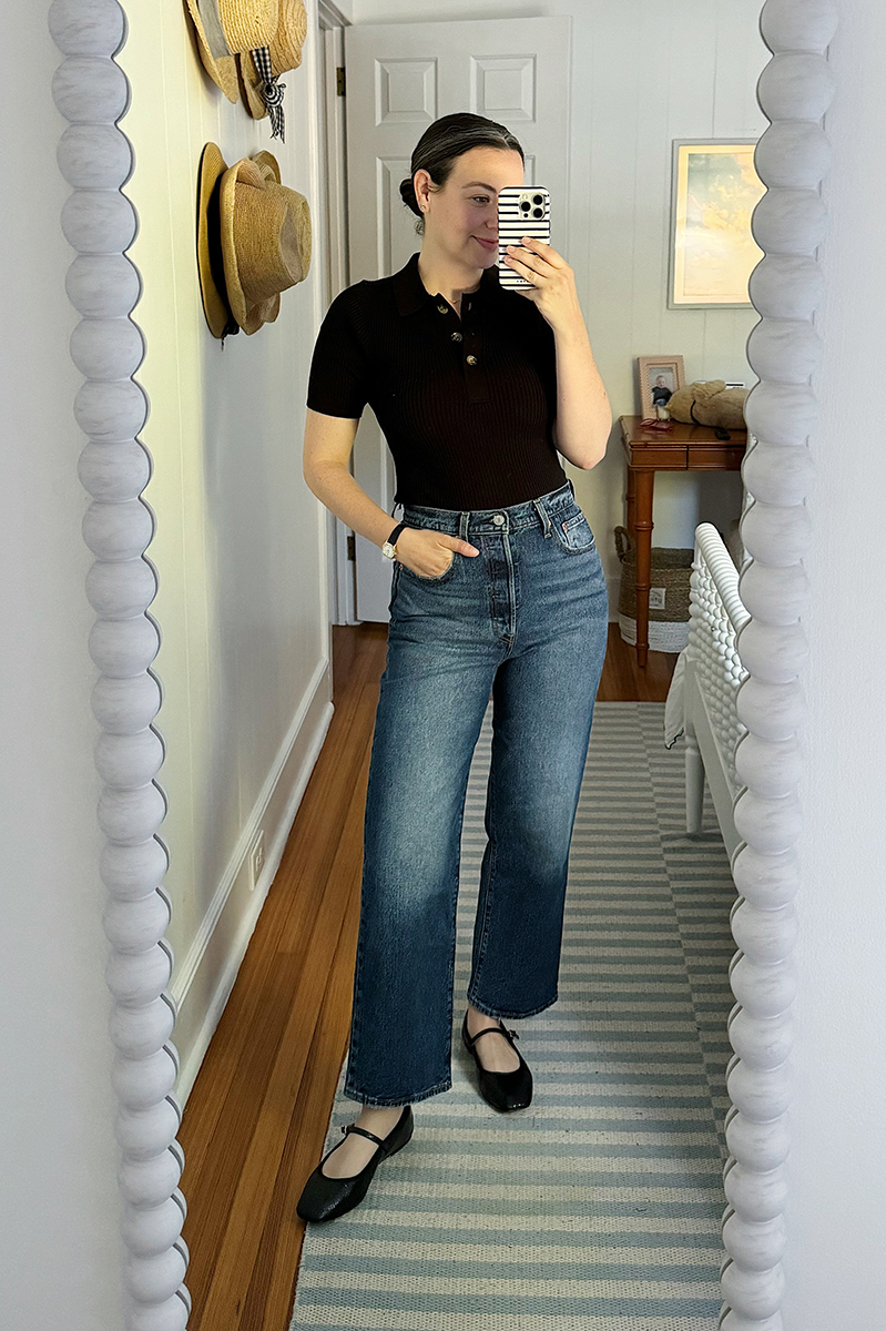 Carly Riordan taking a mirror selfie wearing a black polo and dark denim. 