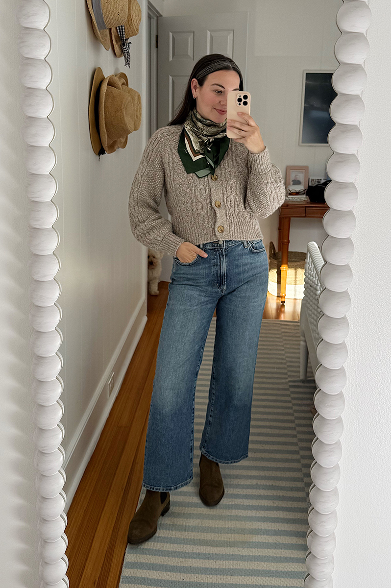 Carly Riordan in a mirror selfie wearing a cardigan, silk scarf, and wide legged jeans.