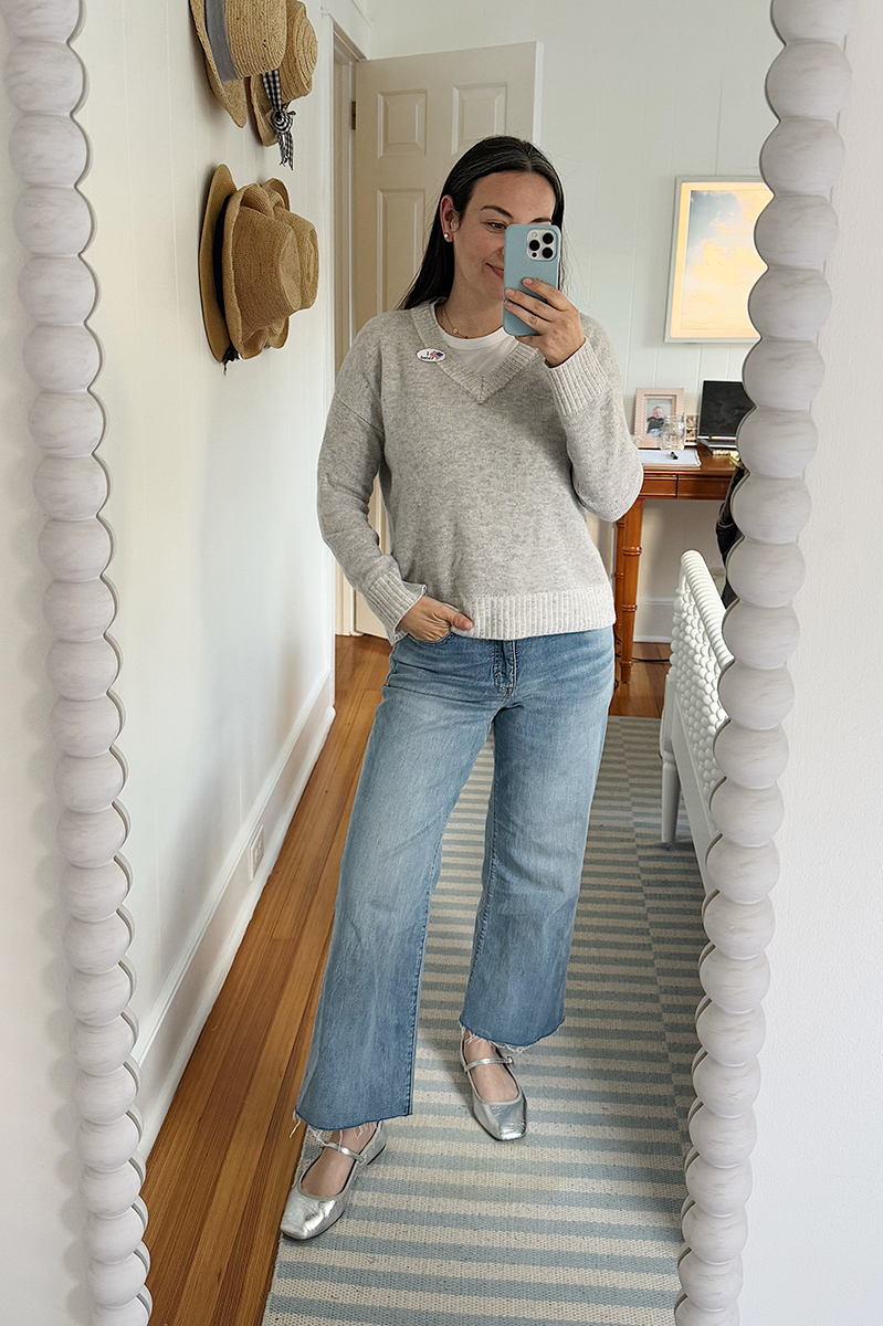 Carly Riordan in a mirror selfie wearing a grey sweater, wide  legged jeans, and metallic ballet flats.