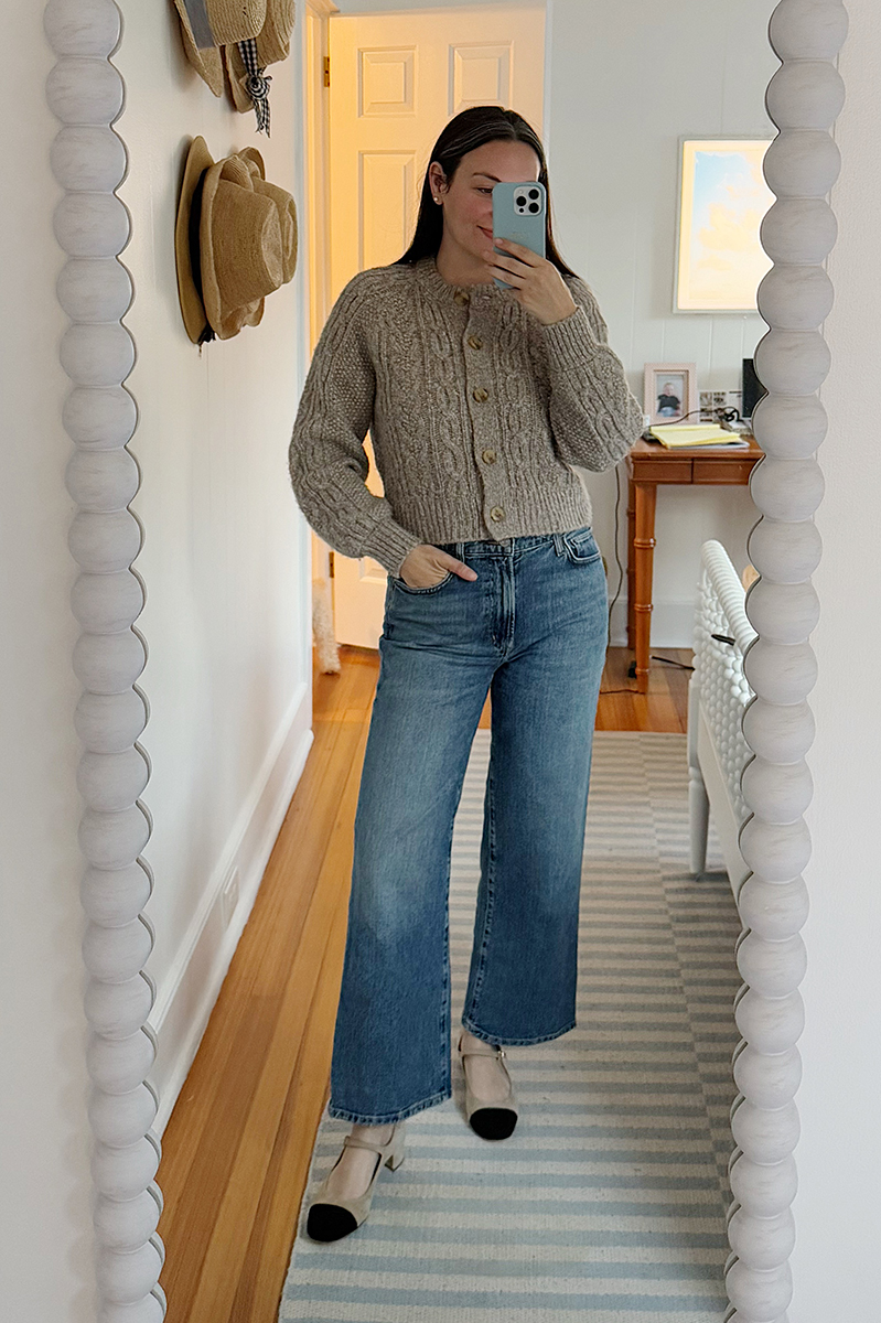 Carly Riordan in a mirror selfie wearing wide legged jeans and a chunky cardigan.