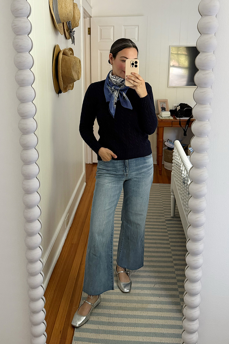 Carly Riordan in a mirror selfie wearing a navy sweater, silk scarf, and metallic mary-janes.