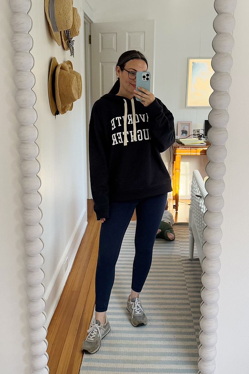 Carly Riordan in a mirror selfie wearing navy leggings and a navy hoodie.