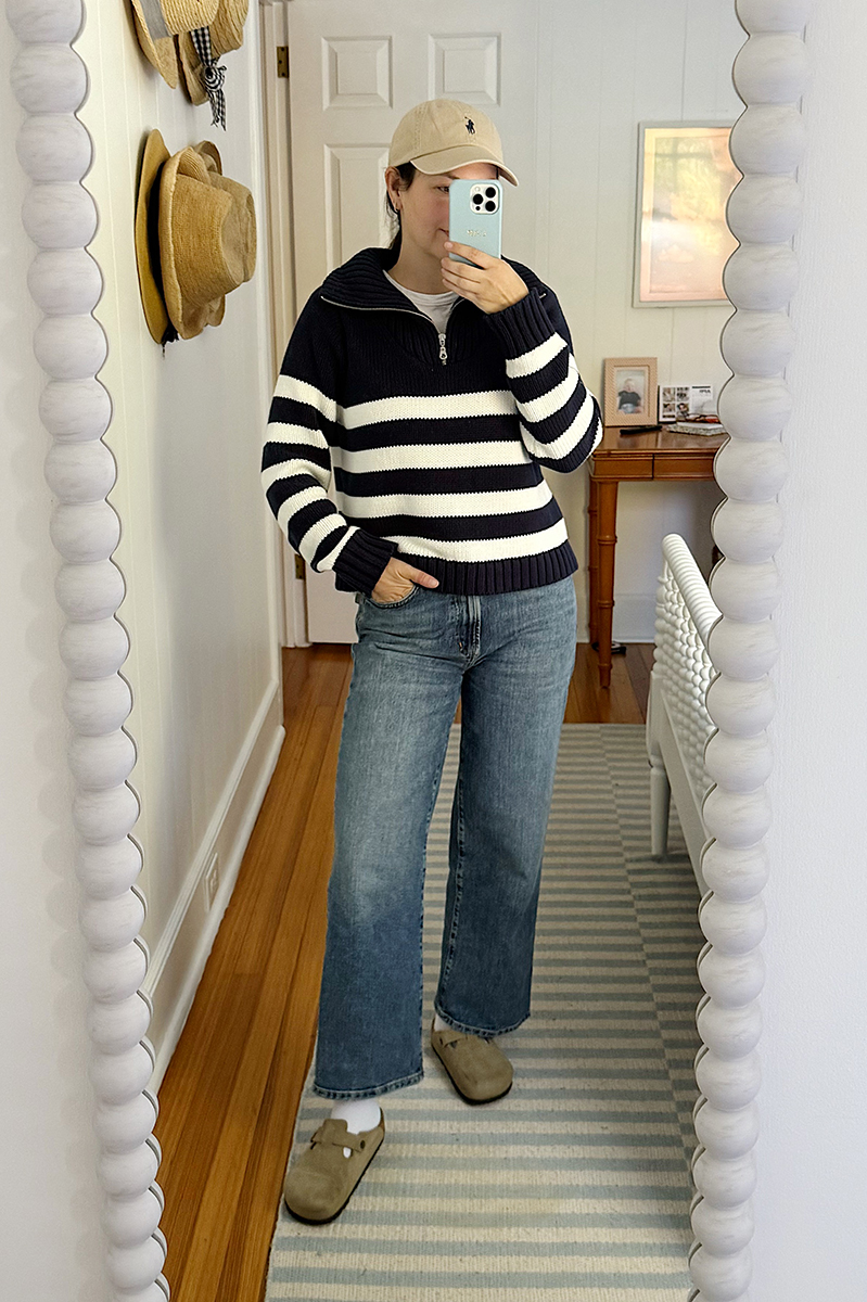 A mirror selfie of Carly Riordan wearing navy and white sweater, wide legged jeans, and clogs.