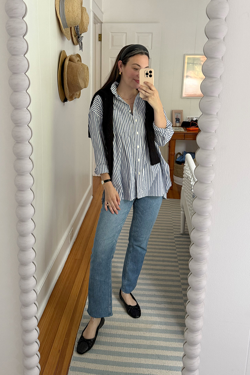 Carly in a mirror selfie wearing blue and white shirt, jeans, and black flats.