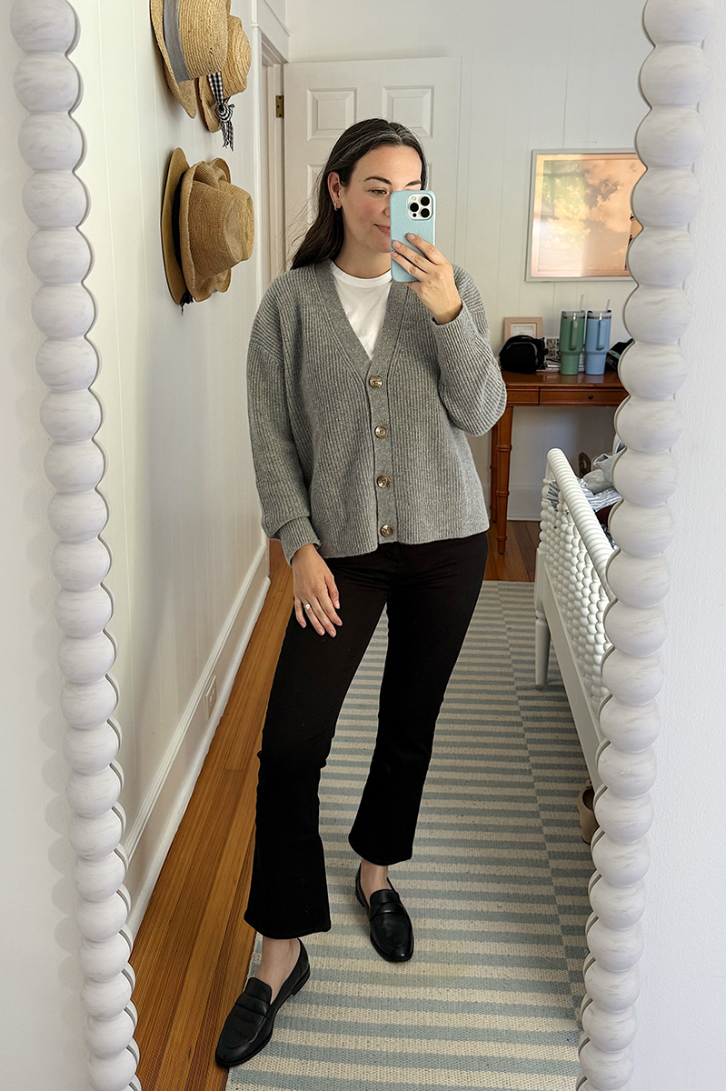 A mirror selfie of Carly Riordan wearing black jeans and a grey cardigan.