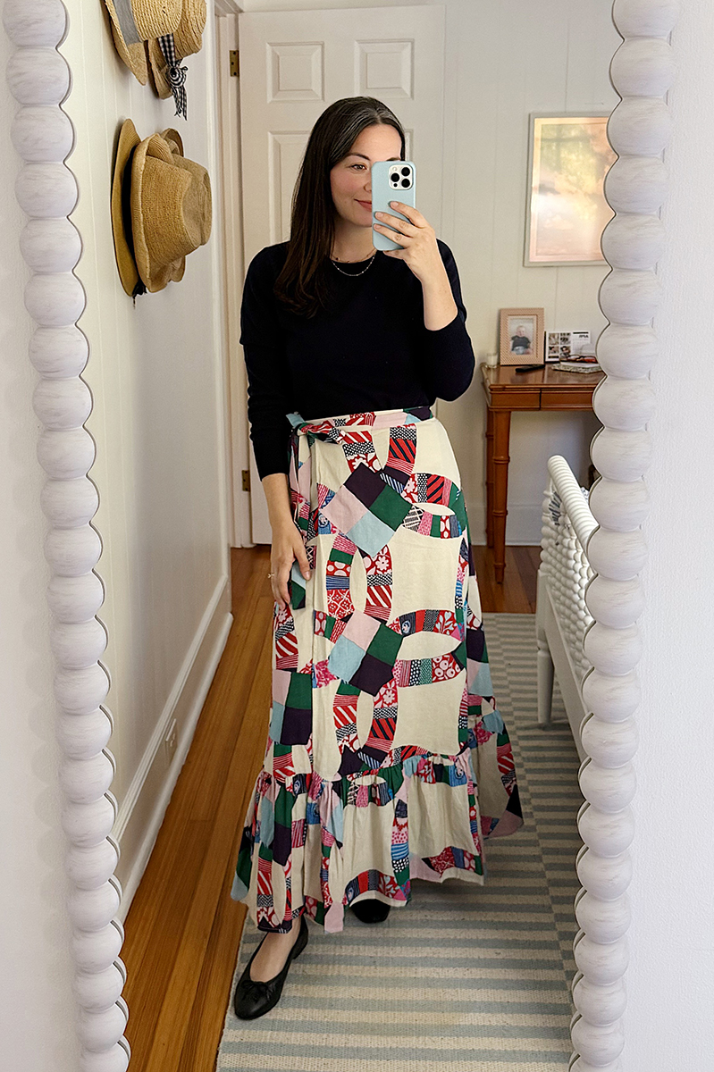 A mirror selfie of Carly Riordan wearing a navy sweater and patchwork skirt.