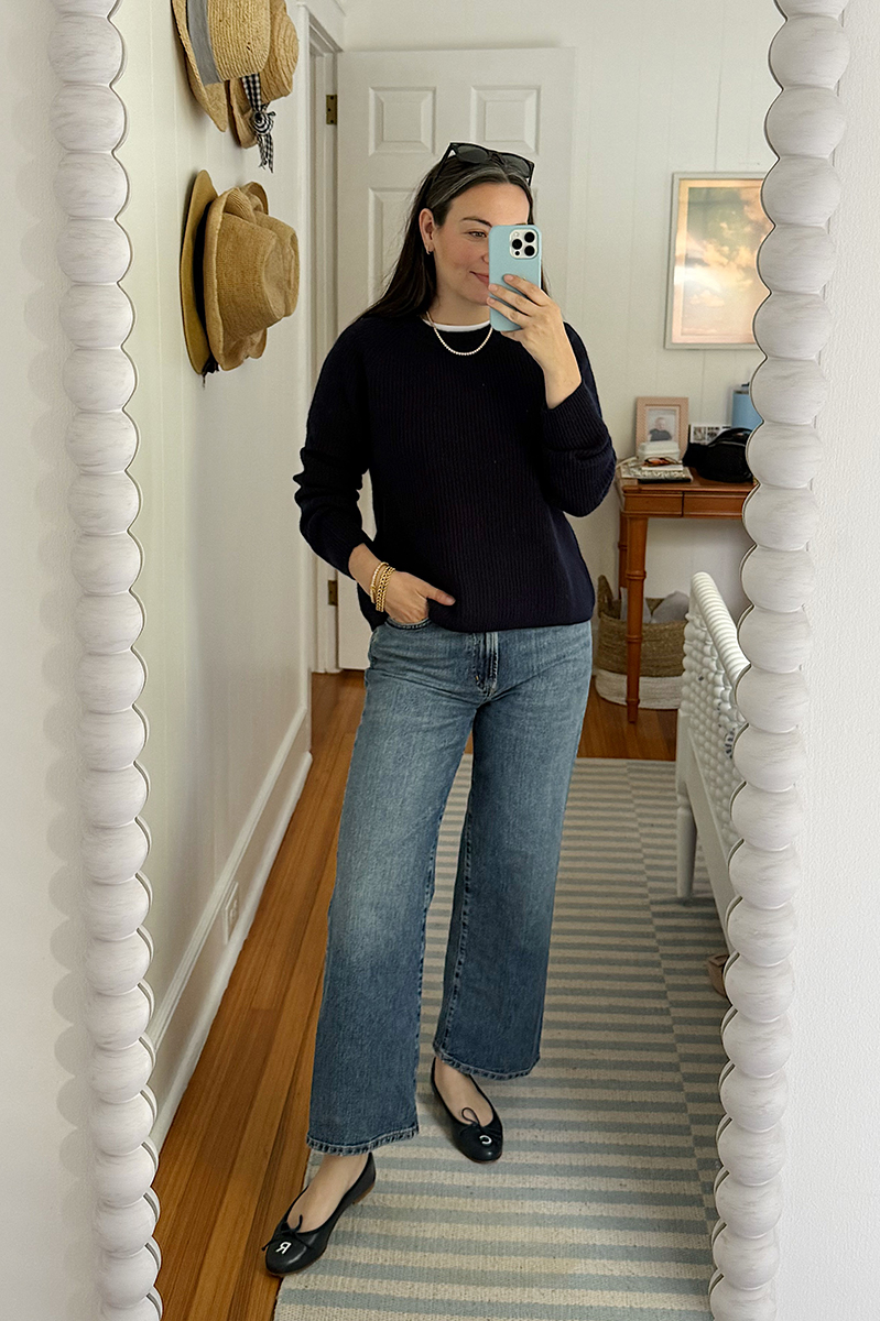 A mirror selfie of Carly Riordan wearing navy and white sweater, wide legged jeans, and clogs.