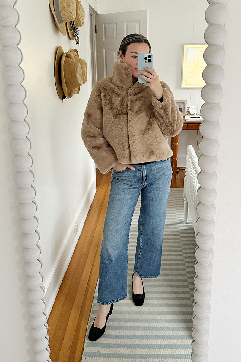 Carly Riordan taking a mirror selfie wearing a faux fur vest and jeans.