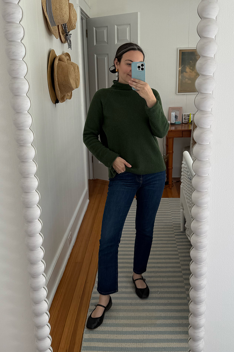 Carly Riordan taking a mirror selfie wearing a green sweater and mary janes.