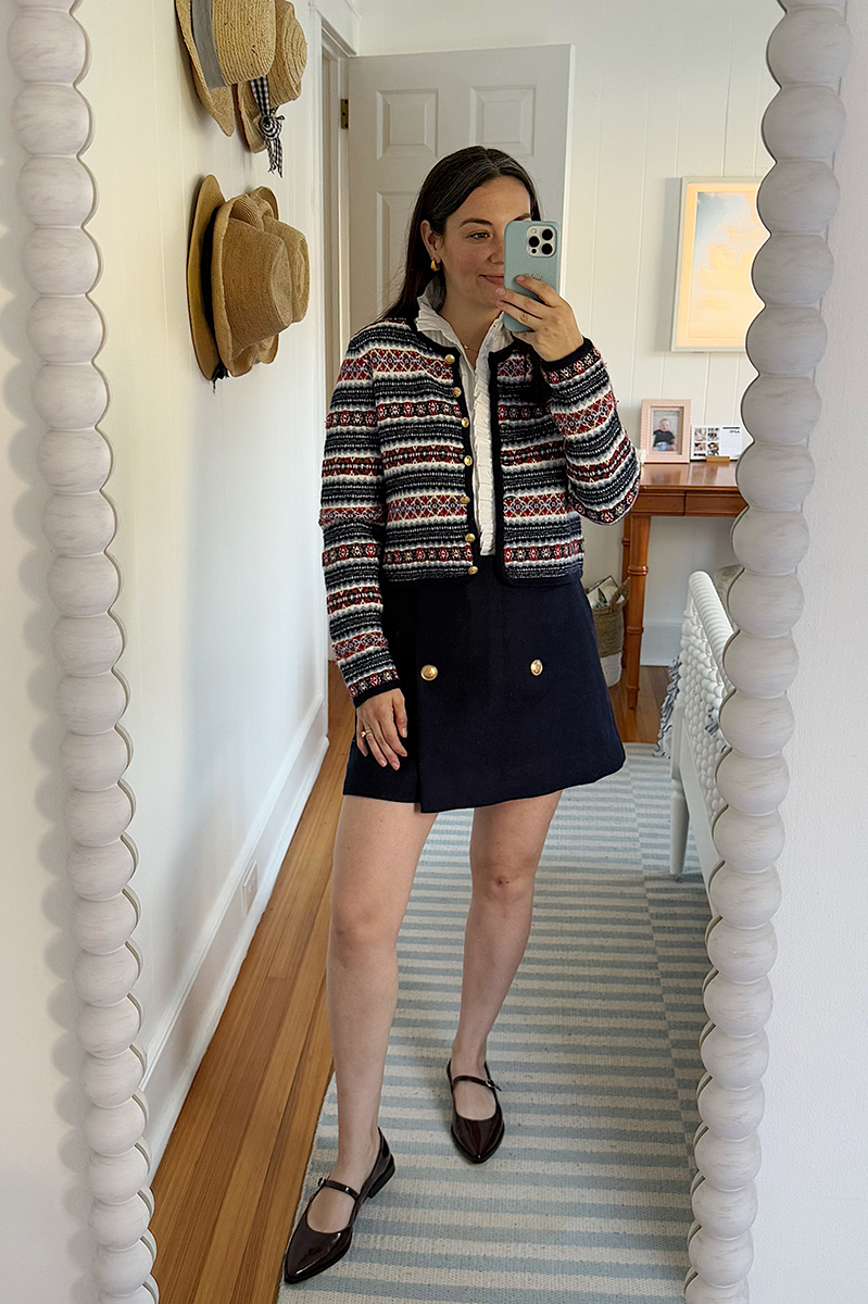 Carly Riordan taking a mirror selfie wearing a fair isle sweater, navy skirt, and burgundy mary janes. 