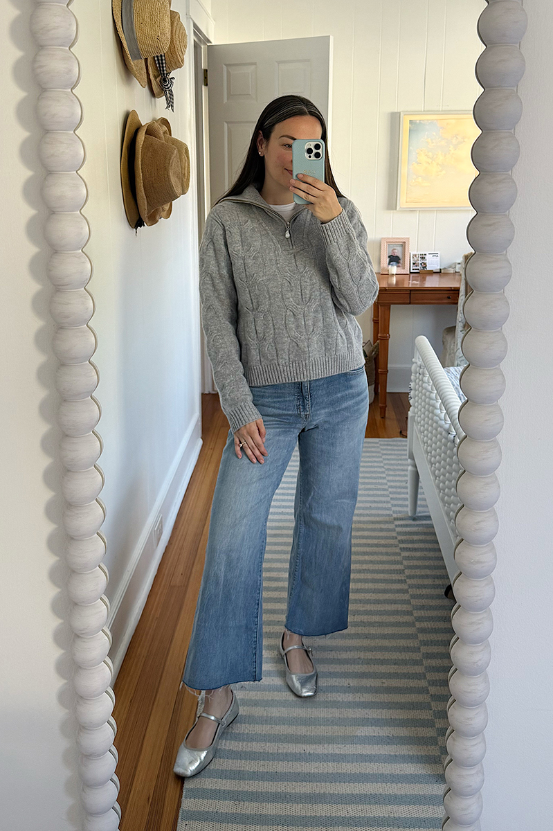 Carly Riordan taking a mirror selfie wearing a grey cashmere pullover and metallic mary janes.