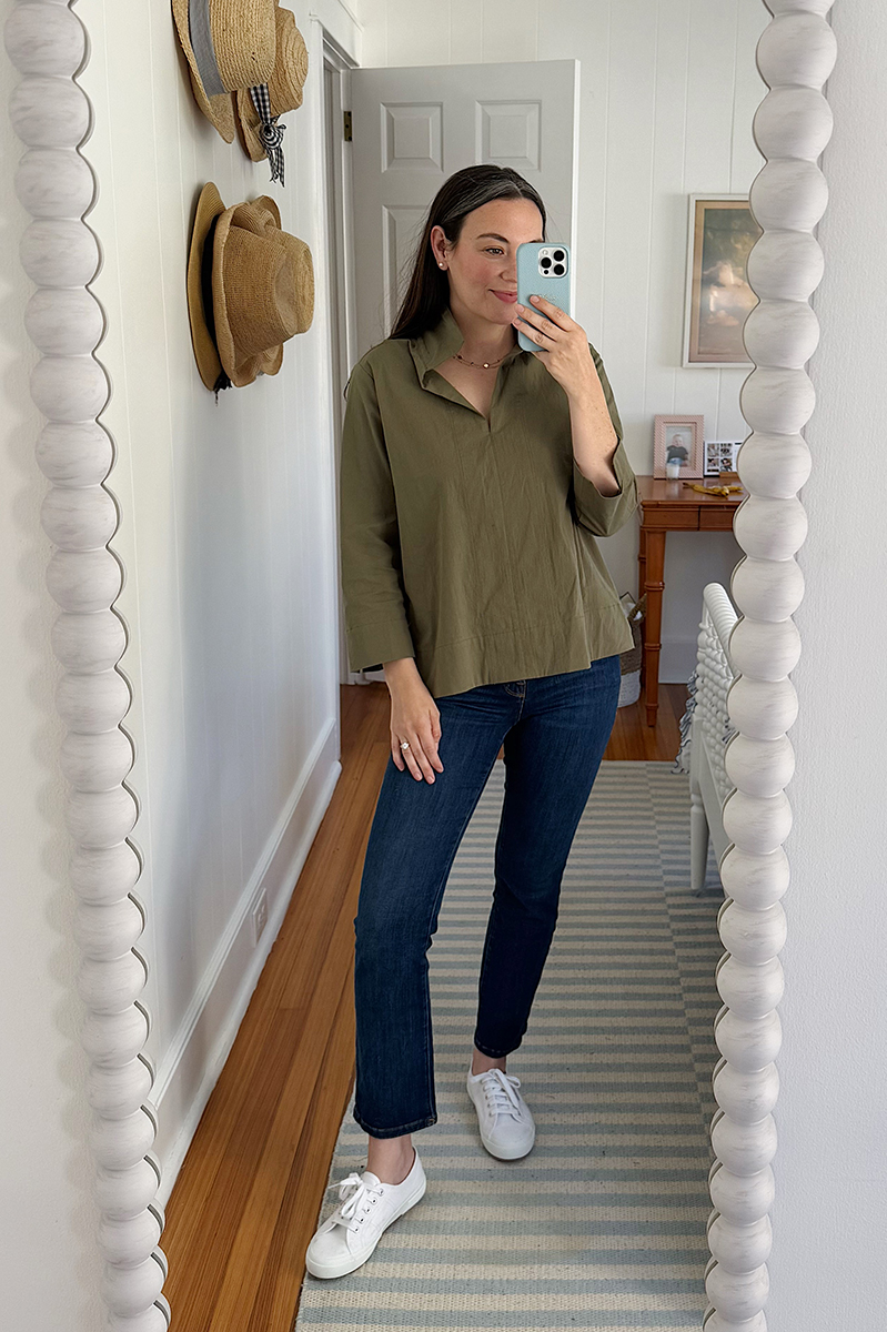 Carly Riordan taking a mirror selfie wearing a green top, dark denim, and white sneakers.