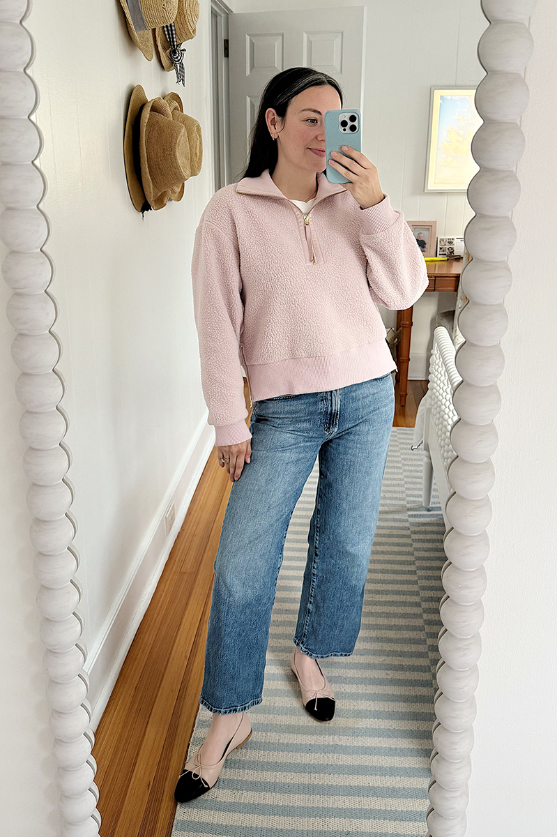 Carly Riordan taking a mirror selfie wearing a fleece pullover and cap toe ballet flats.