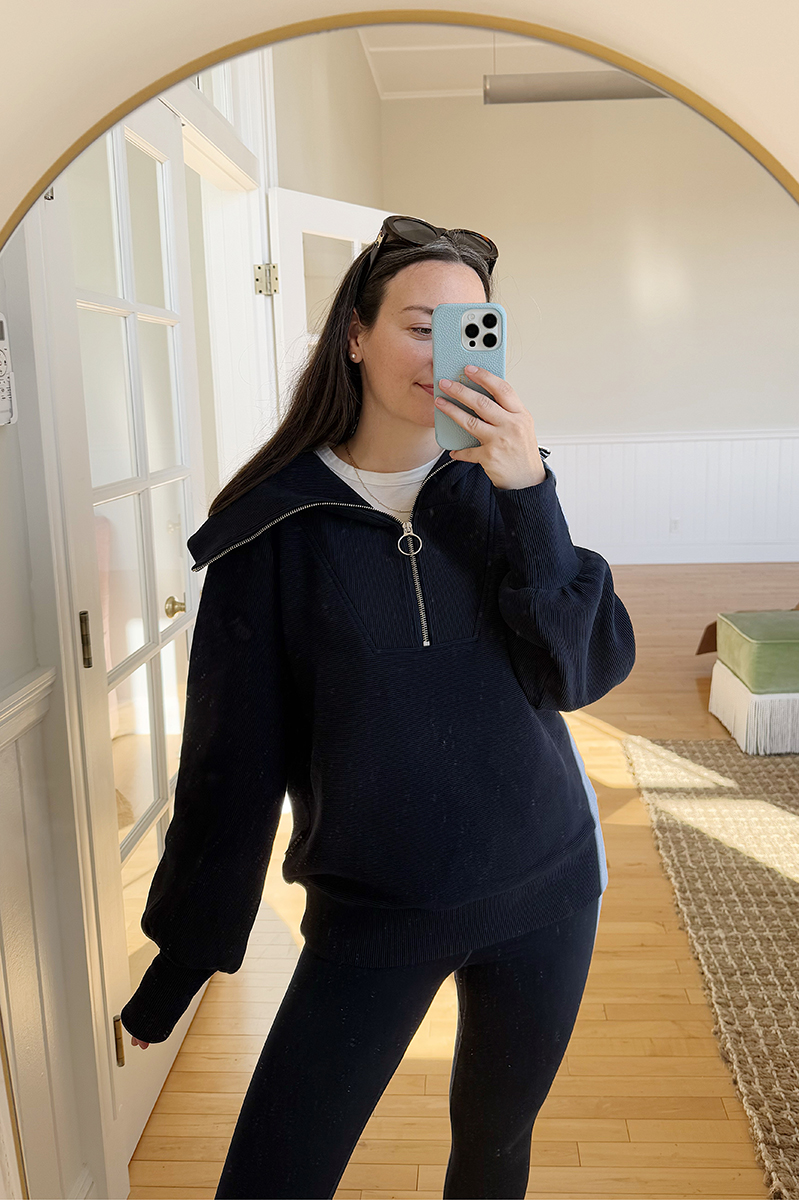 Carly Riordan taking a mirror selfie wearing a navy quarter zip pullover.