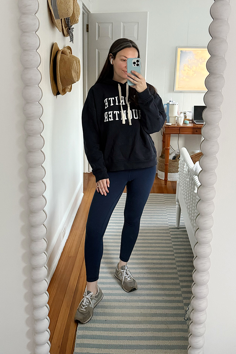 Carly Riordan taking a mirror selfie wearing a Favorite Daughter sweatshirt snd leggings.