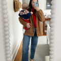 Carly Riordan taking a mirror selfie wearing a barn coat, red sweater and wide legged jeans.