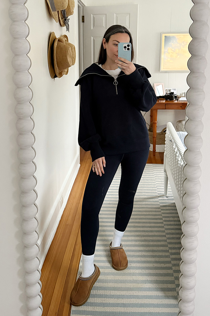 Carly Riordan taking a mirror selfie wearing leggings and a navy pullover.