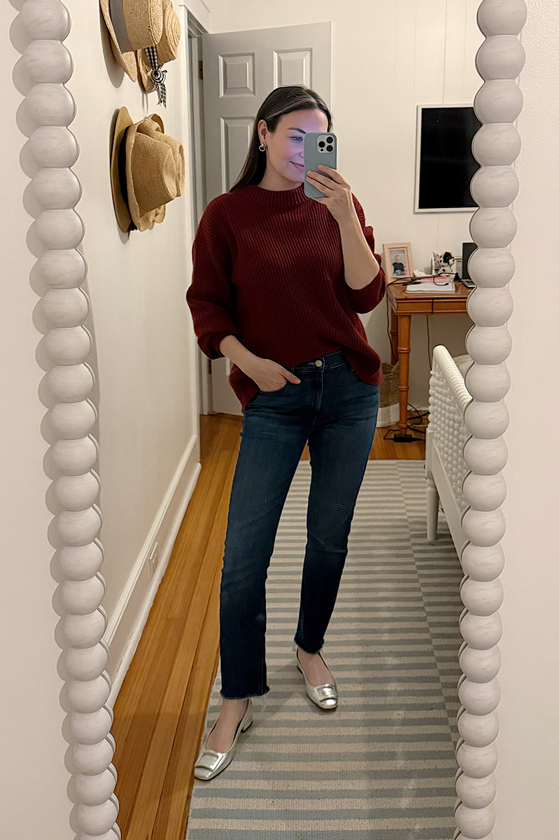 Carly Riordan taking a mirror selfie wearing a maroon sweater and silver flats.