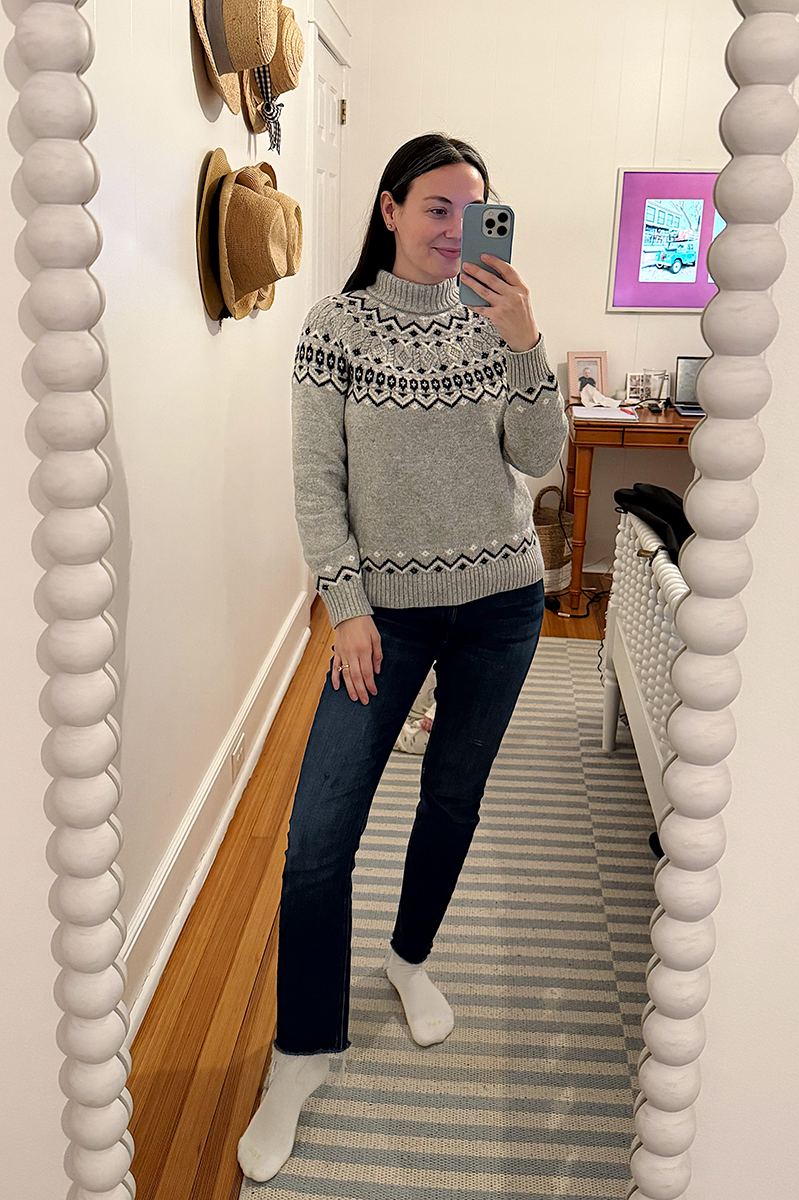 Carly Riordan taking a mirror selfie wearing a grey fair isle sweater and jeans. 