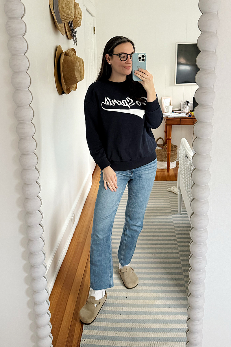 Carly Riordan taking a mirror selfie wearing a "go sports" sweatshirt and jeans.