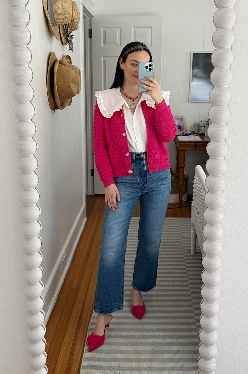 Carly Riordan taking a mirror selfie wearing a pink cardigan, jeans, and pink mules.