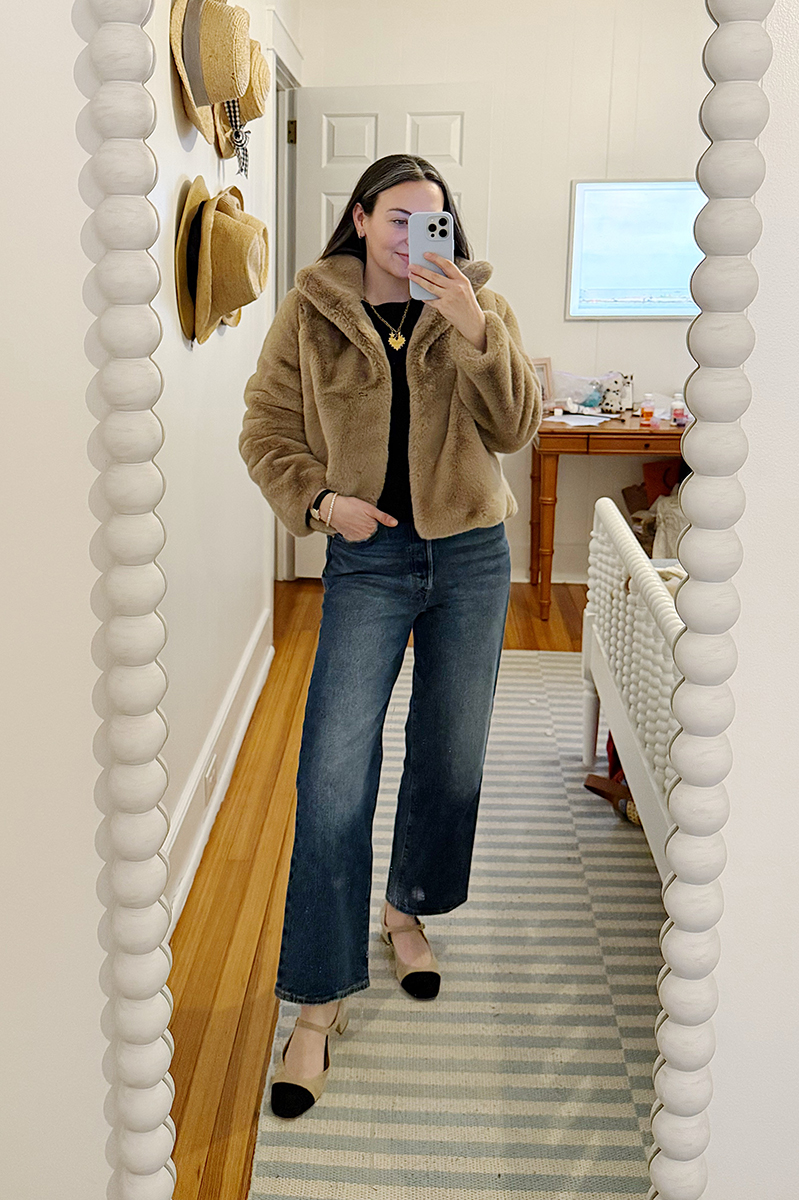 Carly Riordan taking a mirror selfie wearing a faux fur jacket and cap toe heels. 