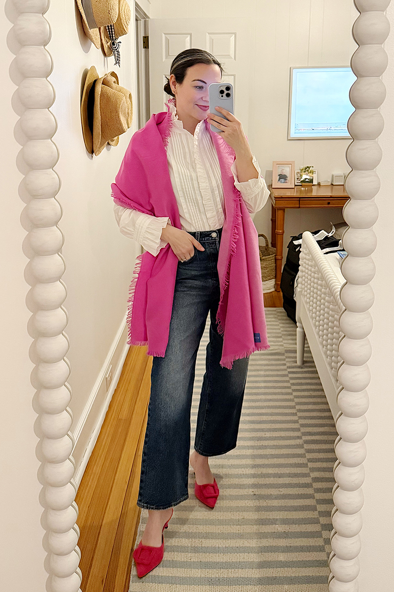 Carly Riordan taking a mirror selfie wearing a pink scarf, jeans, and a button down.