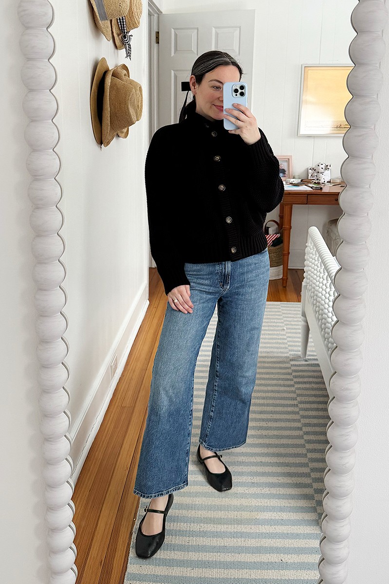 Carly Riordan taking a mirror selfie wearing a black cardigan and mary janes. 