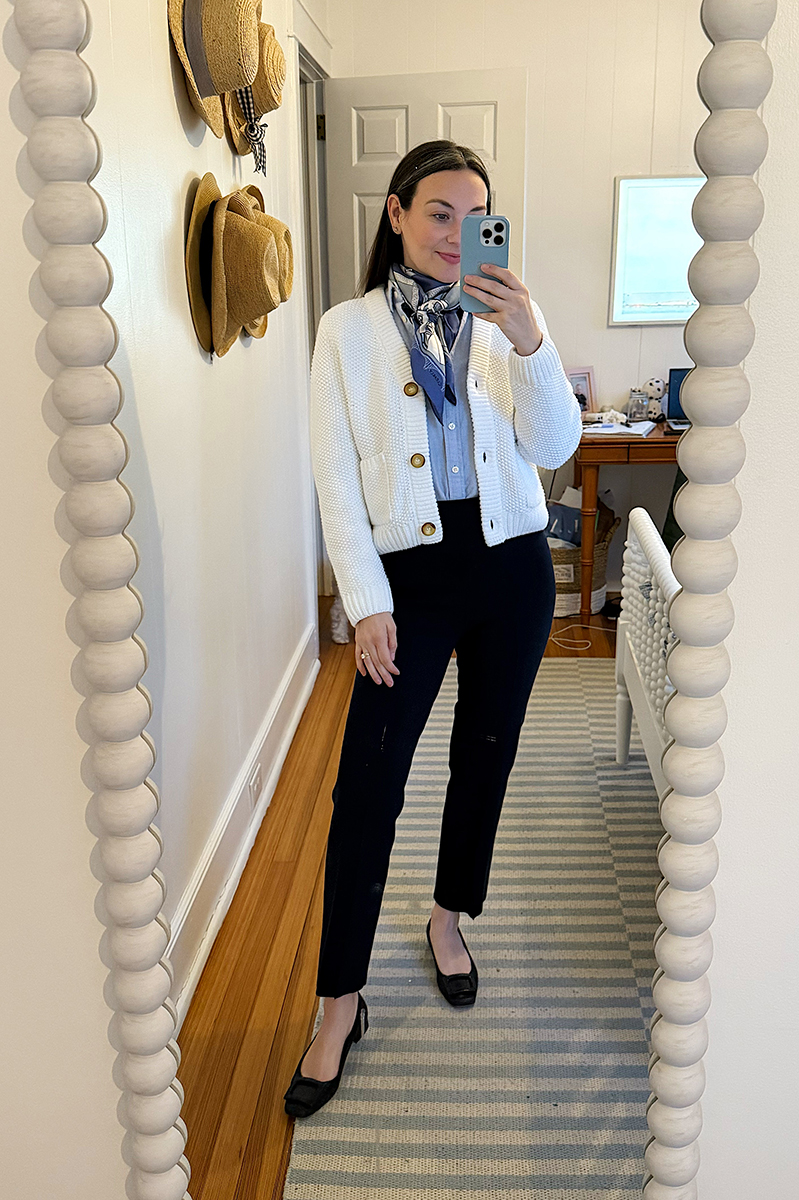 Carly taking a mirror selfie wearing a white cardigan and navy pants