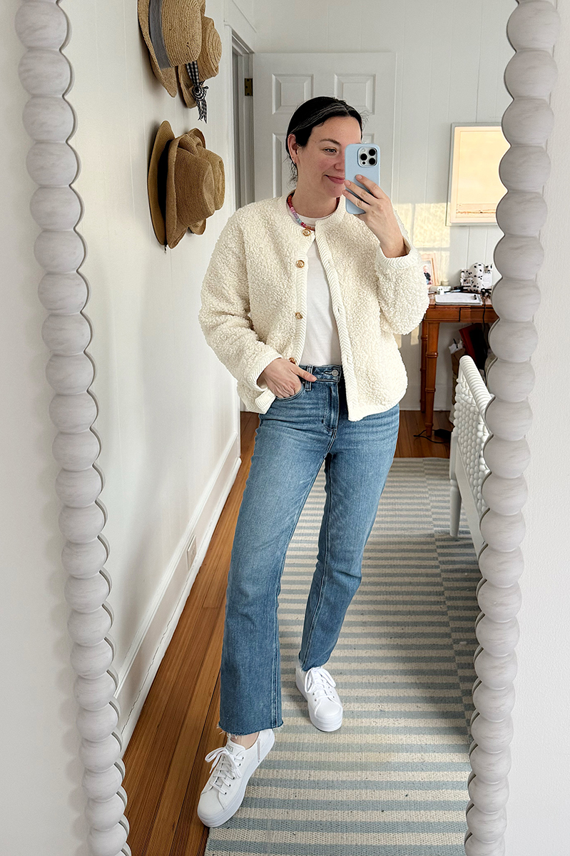 Carly taking a mirror selfie wearing a white jacket and jeans