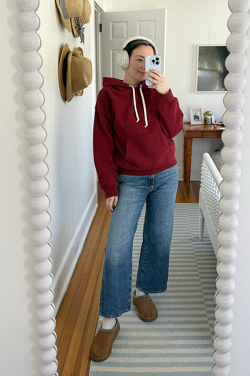 Carly Riordan taking a mirror selfie wearing a red hoodie and wide leg jeans. 