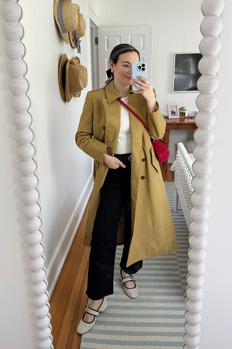 Carly Riordan taking a mirror selfie wearing a J. Crew long trench coat and black jeans. 