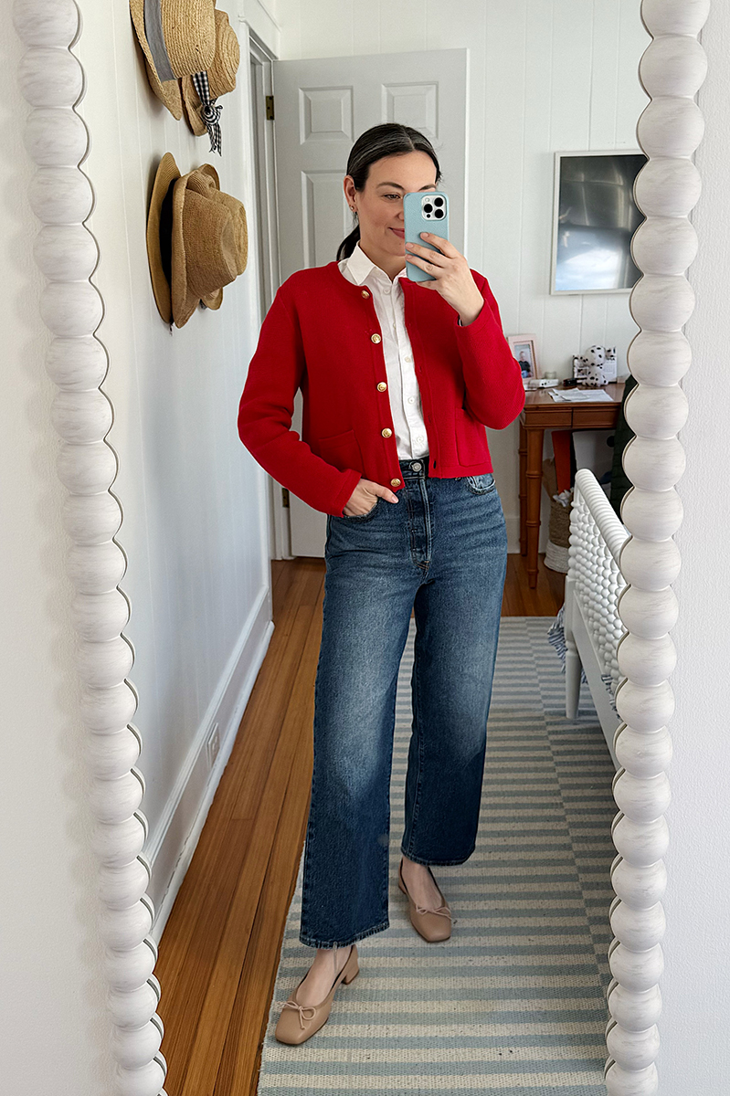 Carly taking a mirror selfie wearing a red lady jacket and white leg jeans.