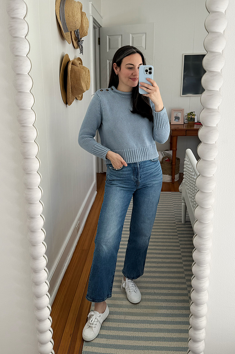 Carly Riordan taking a mirror selfie wearing a blue sweater and jeans.