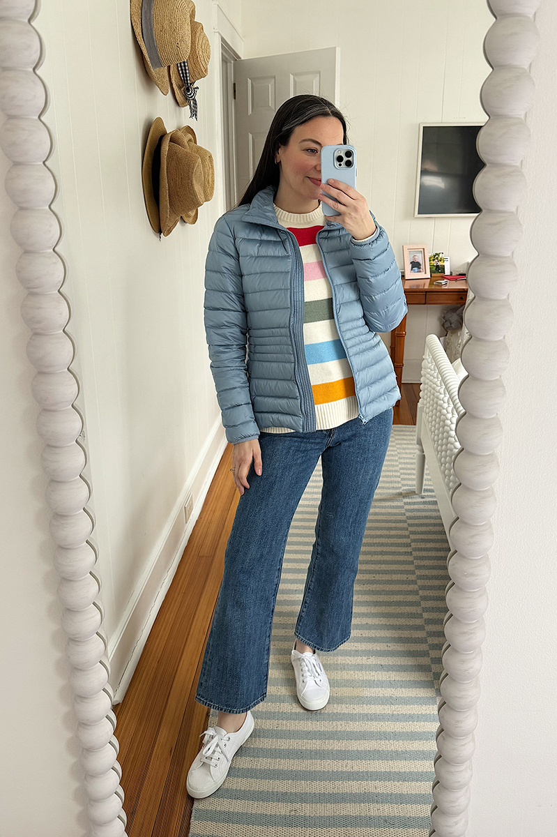 Carly Riordan taking a mirror selfie wearing a stripe sweater and a blue puffer coat.