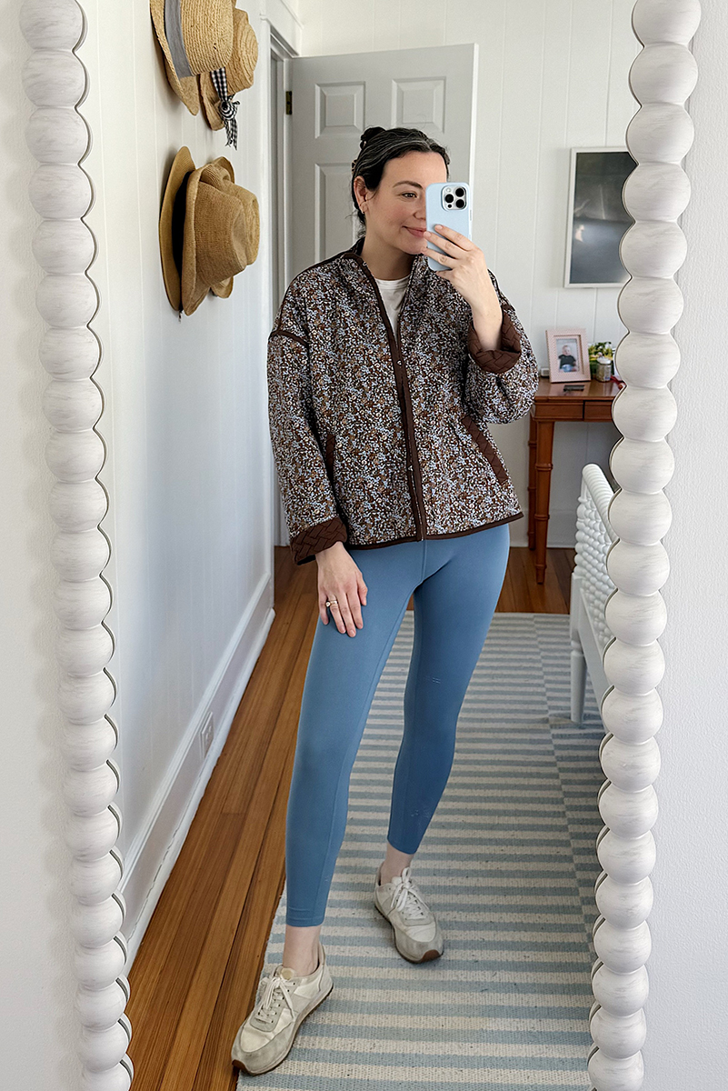 Carly Riordan taking a mirror selfie wearing a reversible floral quilted jacket and leggings.