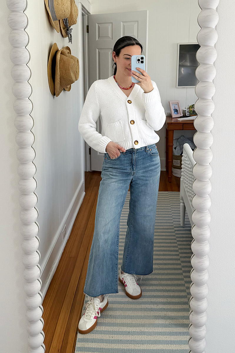 Carly Riordan taking a mirror selfie wearing a cardigan and wide legged jeans. 