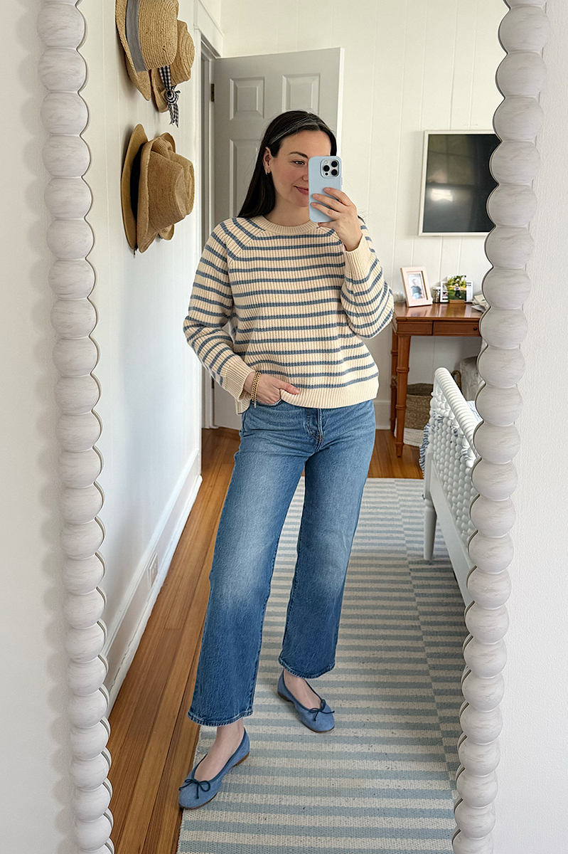 Carly Riordan taking a mirror selfie wearing a striped sweater and denim ballet flats.